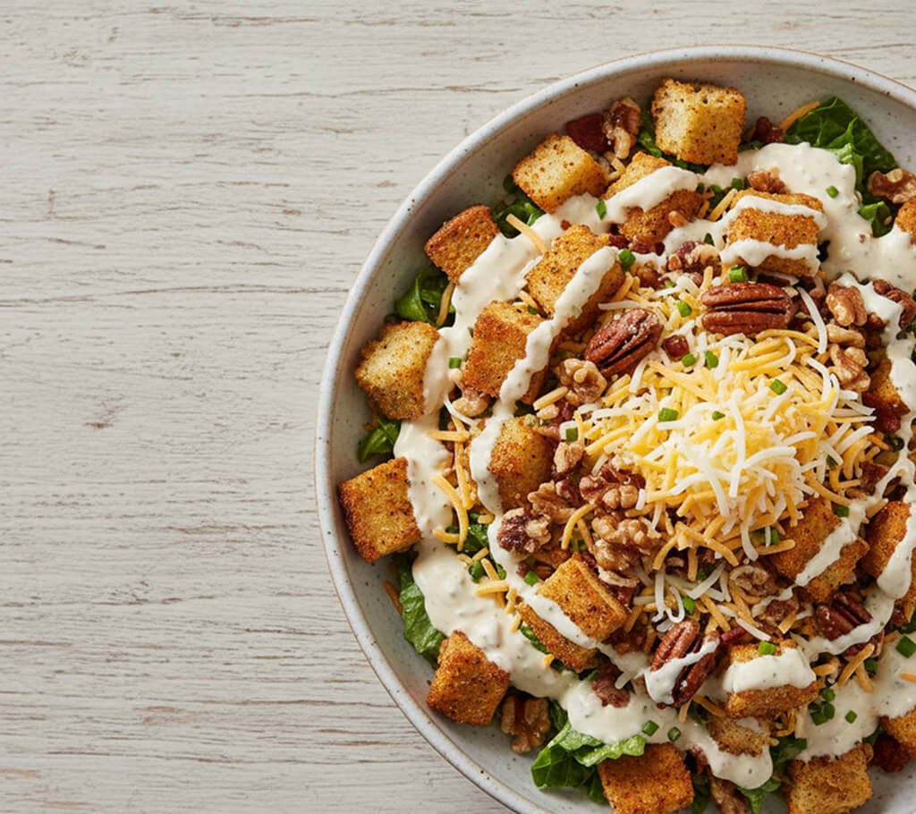 A salad loaded with creamy dressing, croutons, cheese, and candied nuts